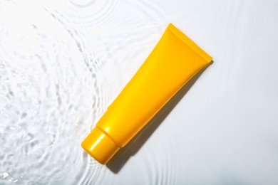 Cosmetic product. Tube with cream in water on light background, top view