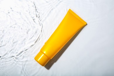 Cosmetic product. Tube with cream in water on light background, top view