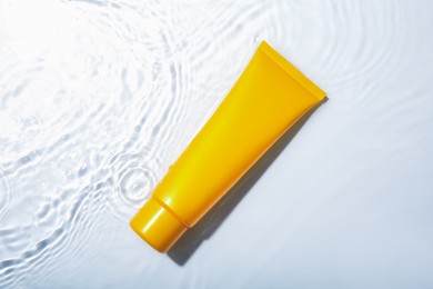 Photo of Cosmetic product. Tube with cream in water on light background, top view