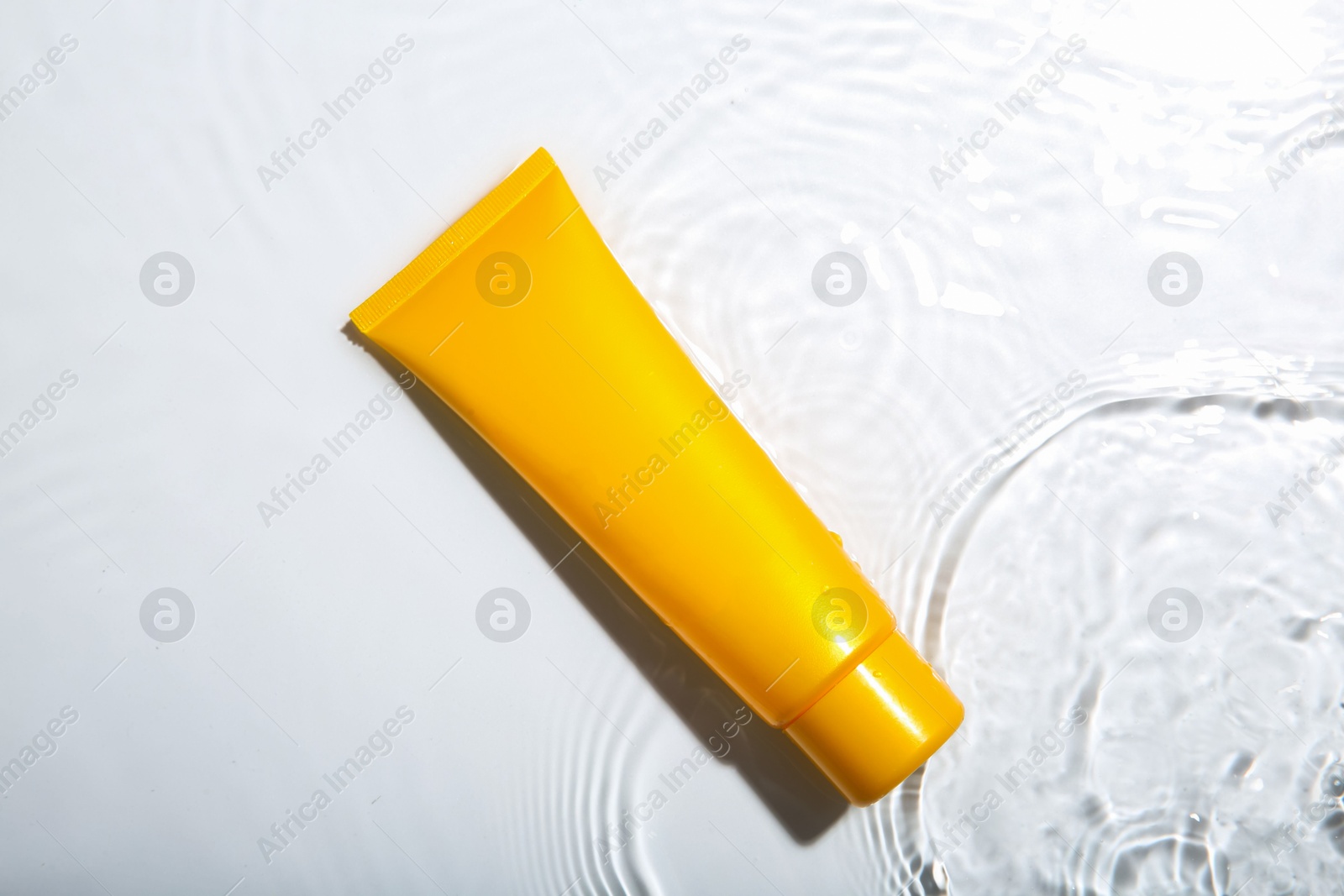 Photo of Cosmetic product. Tube with cream in water on light background, top view