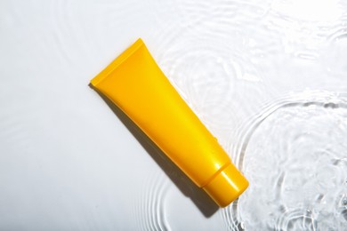 Photo of Cosmetic product. Tube with cream in water on light background, top view