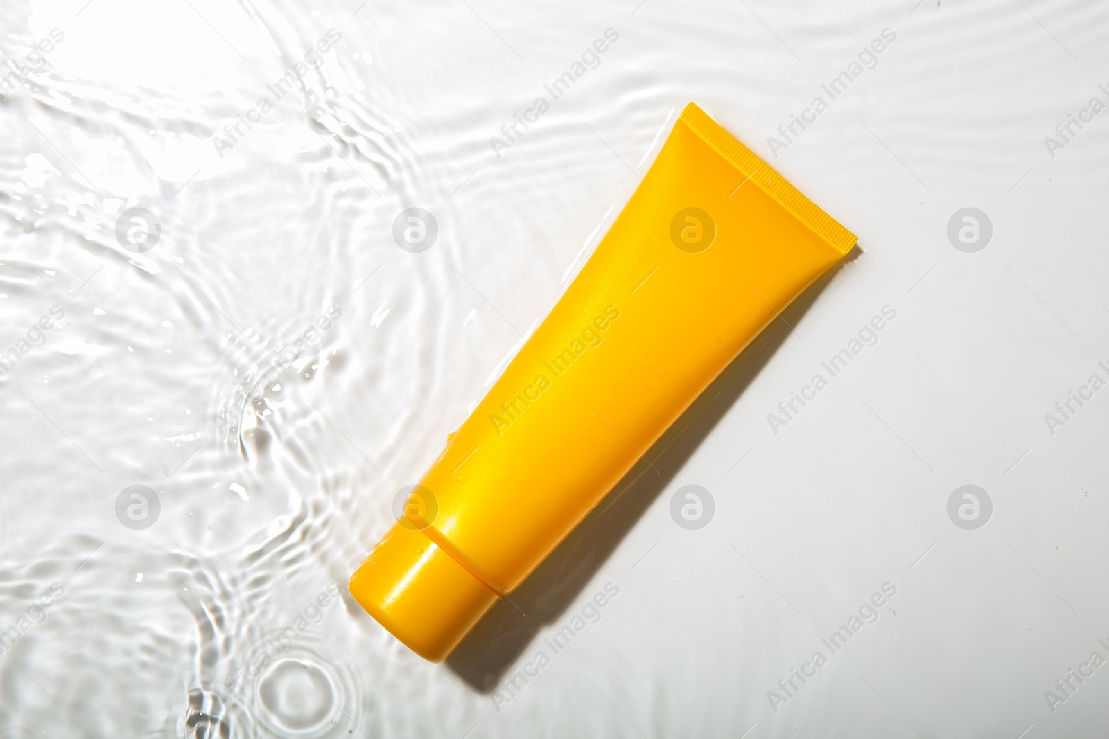 Photo of Cosmetic product. Tube with cream in water on light background, top view