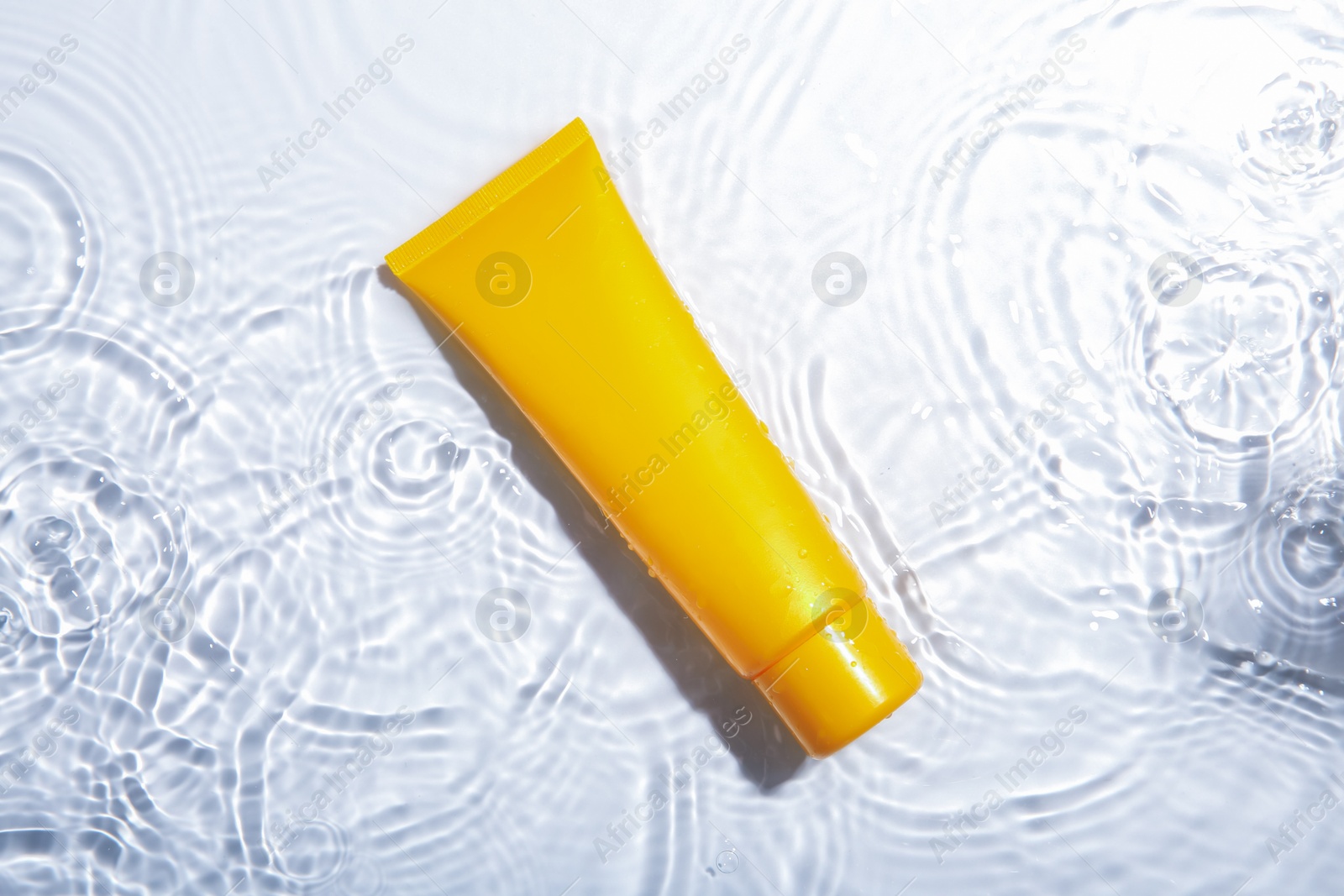 Photo of Cosmetic product. Tube with cream in water on light background, top view