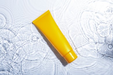 Photo of Cosmetic product. Tube with cream in water on light background, top view