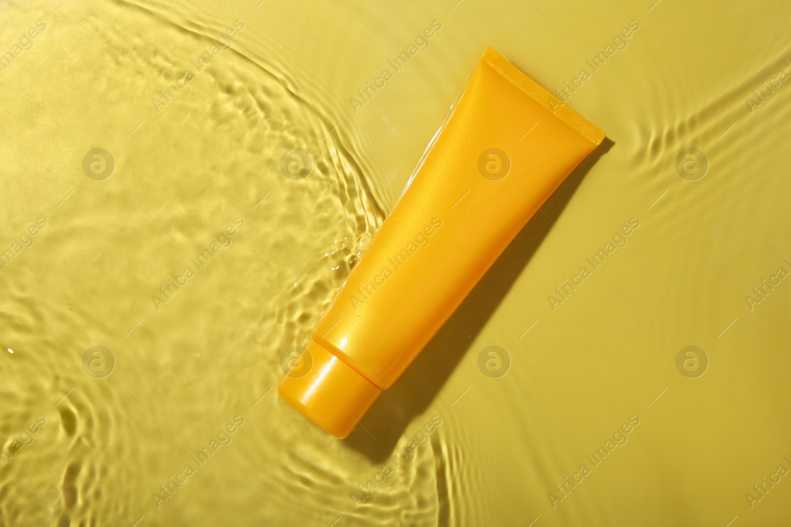 Photo of Tube with cream in water on yellow background, top view. Cosmetic product