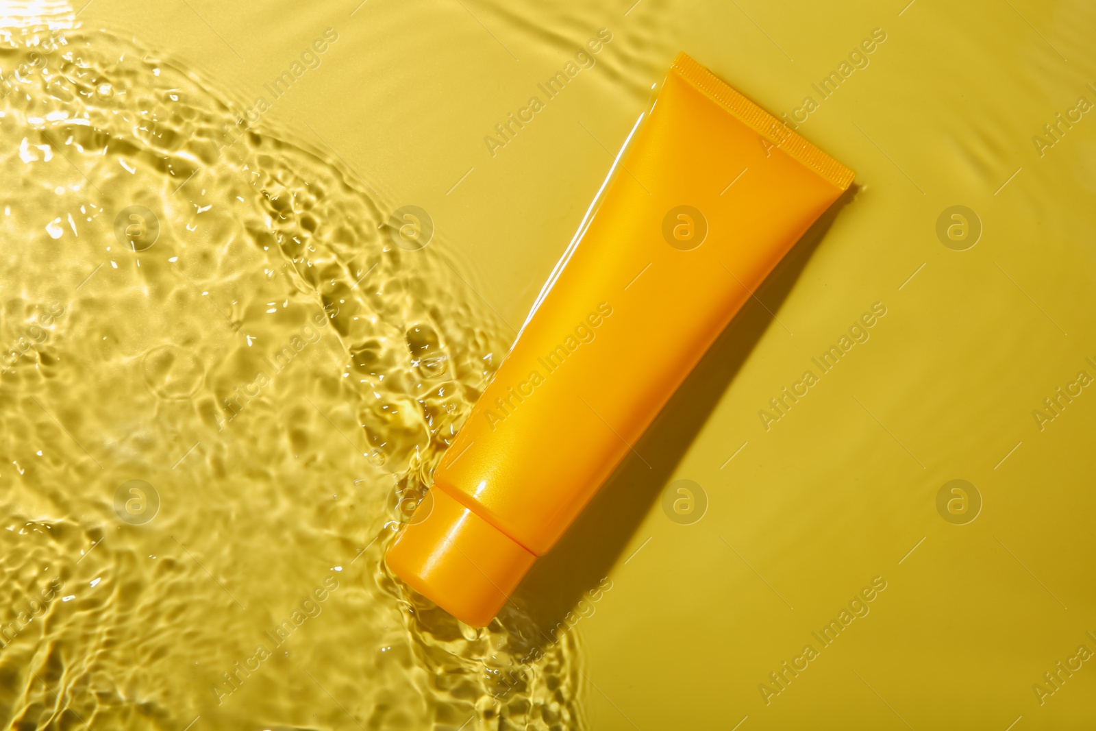 Photo of Tube with cream in water on yellow background, top view. Cosmetic product