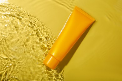 Tube with cream in water on yellow background, top view. Cosmetic product