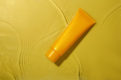 Photo of Tube with cream in water on yellow background, top view. Cosmetic product