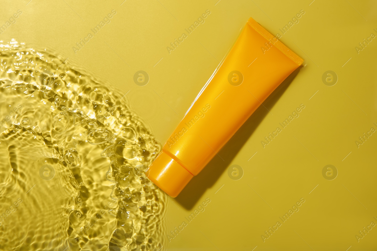 Photo of Tube with cream in water on yellow background, top view. Cosmetic product