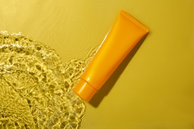 Photo of Tube with cream in water on yellow background, top view. Cosmetic product