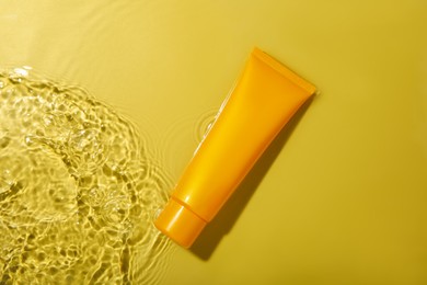 Tube with cream in water on yellow background, top view. Cosmetic product