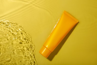 Tube with cream in water on yellow background, top view. Cosmetic product