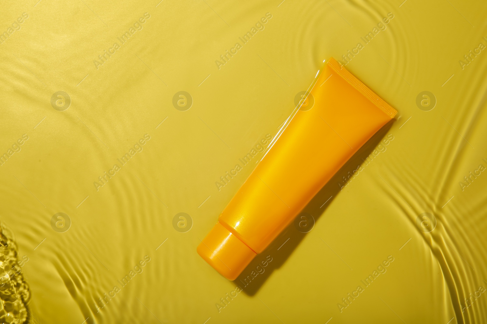 Photo of Tube with cream in water on yellow background, top view. Cosmetic product