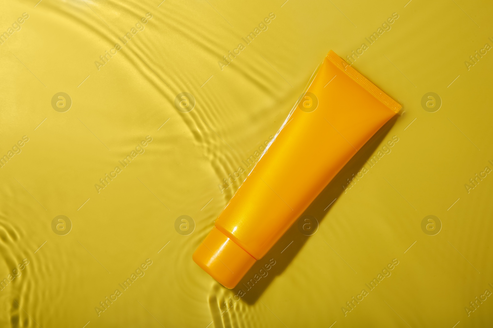 Photo of Tube with cream in water on yellow background, top view. Cosmetic product