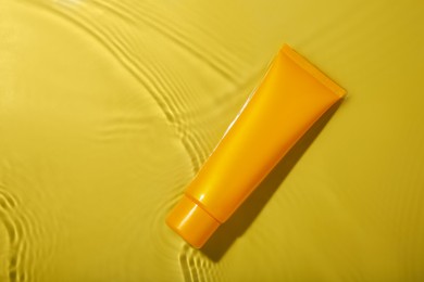 Photo of Tube with cream in water on yellow background, top view. Cosmetic product