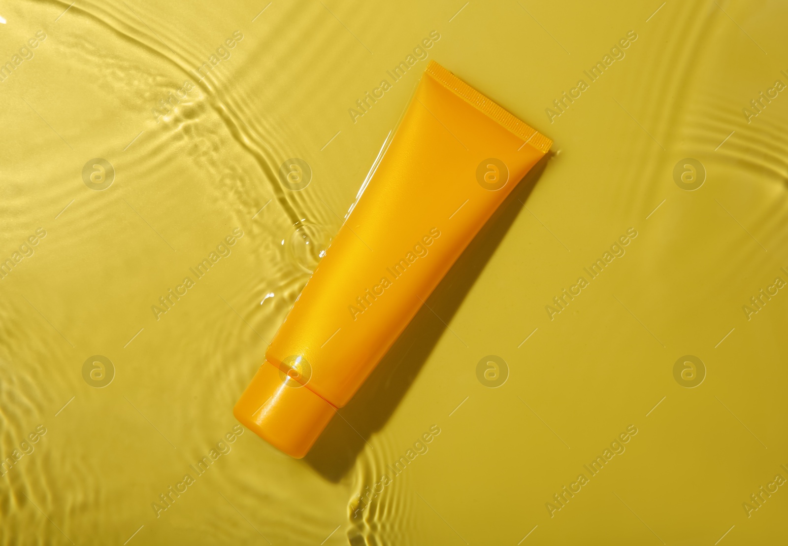 Photo of Tube with cream in water on yellow background, top view. Cosmetic product