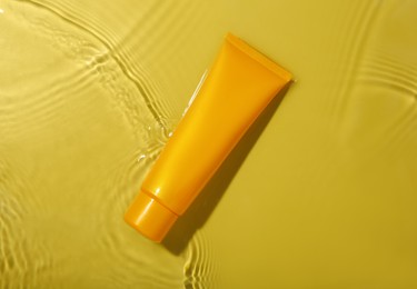 Tube with cream in water on yellow background, top view. Cosmetic product