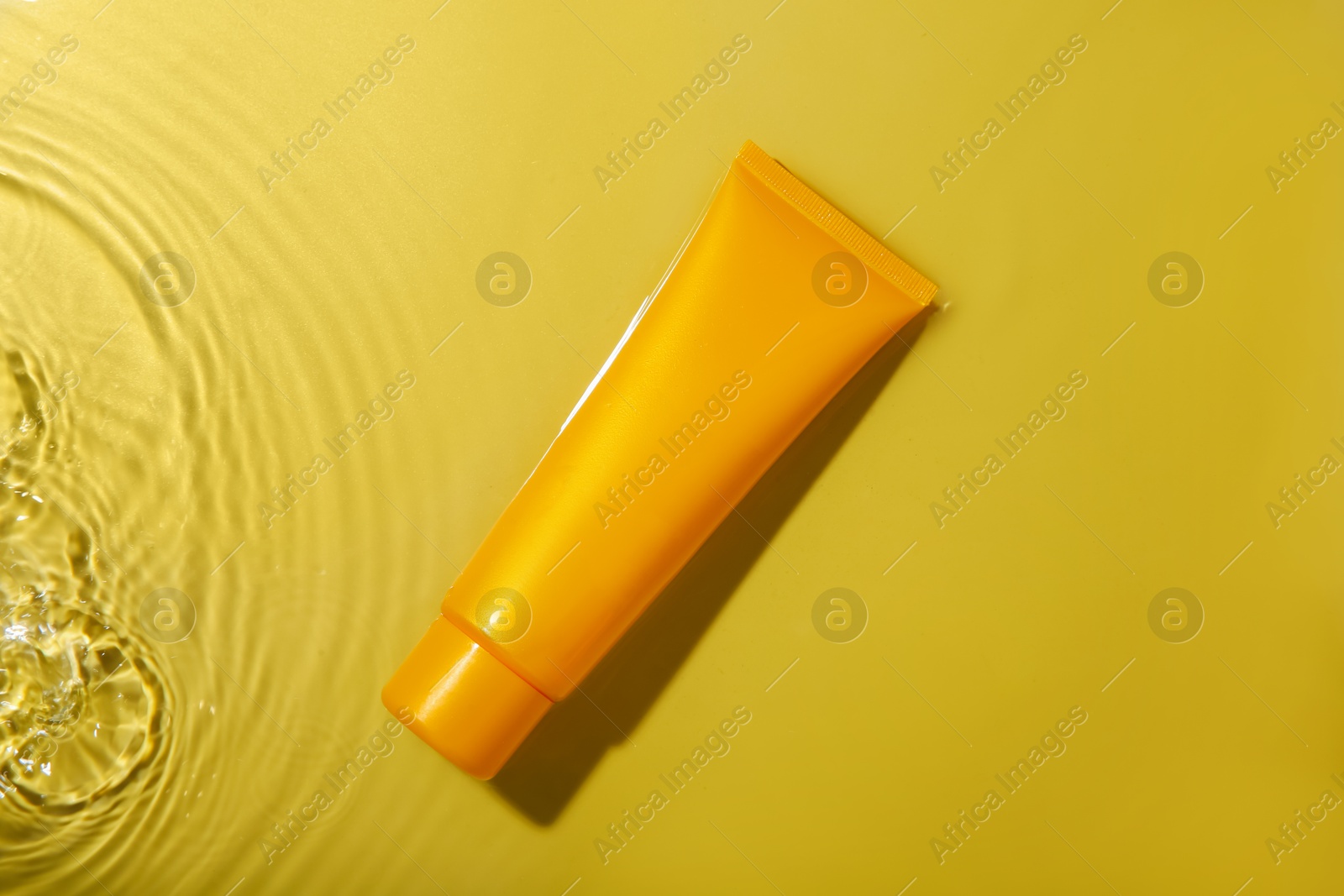 Photo of Tube with cream in water on yellow background, top view. Cosmetic product