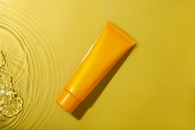 Photo of Tube with cream in water on yellow background, top view. Cosmetic product