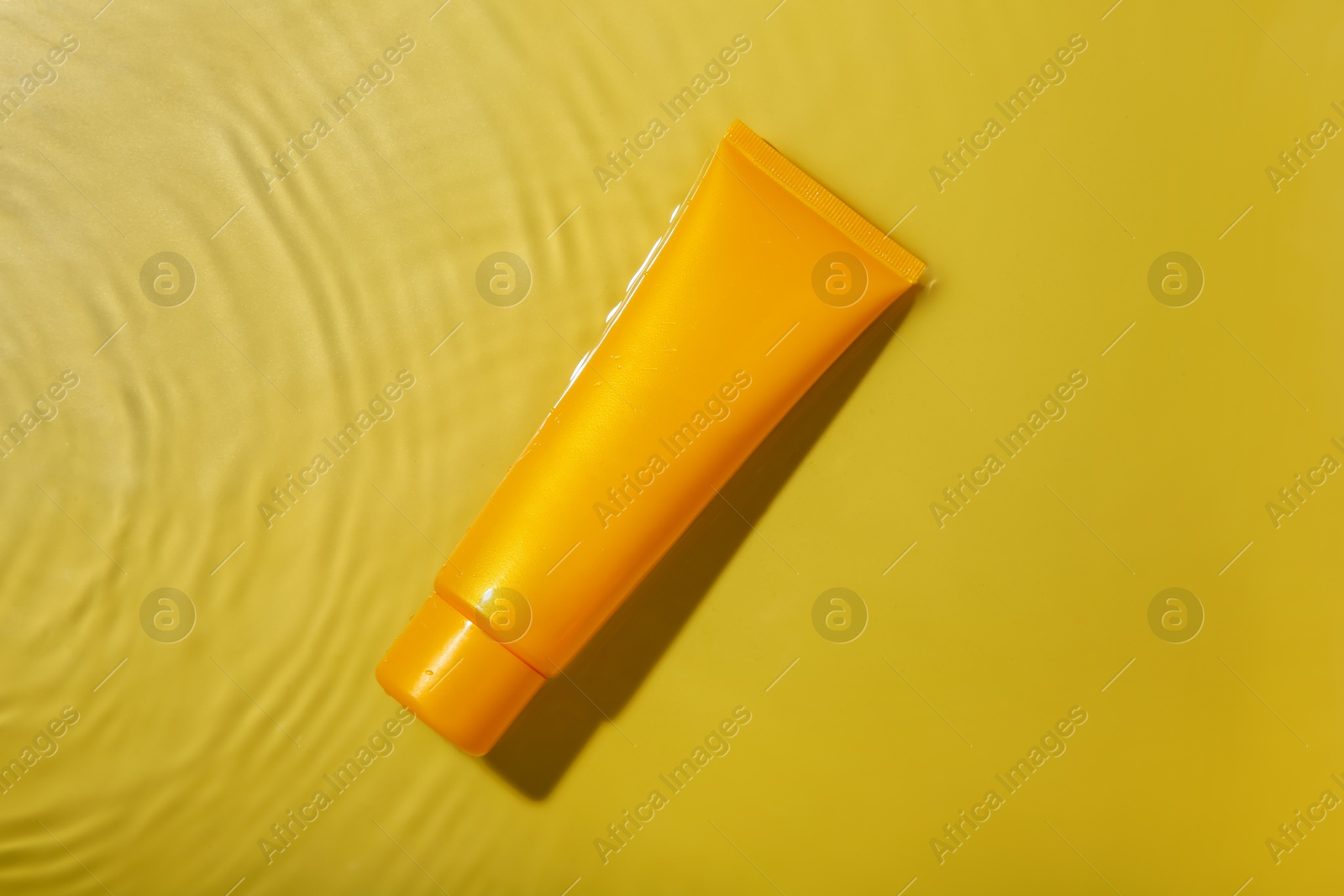 Photo of Tube with cream in water on yellow background, top view. Cosmetic product