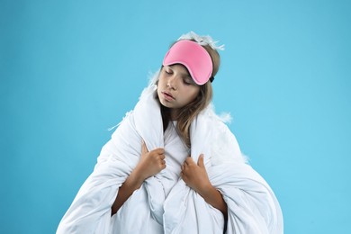 Photo of Overslept girl with sleep mask wrapped in blanket on light blue background