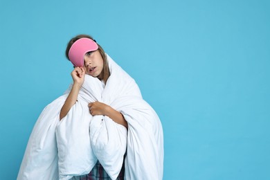 Photo of Overslept girl with sleep mask wrapped in blanket on light blue background, space for text