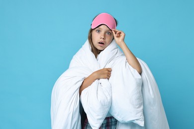 Overslept girl with sleep mask wrapped in blanket on light blue background