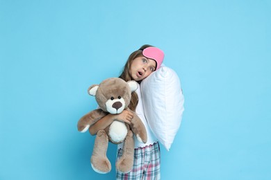 Photo of Overslept girl with sleep mask, pillow and teddy bear on light blue background