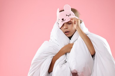 Overslept girl with sleep mask wrapped in blanket on pink background, space for text