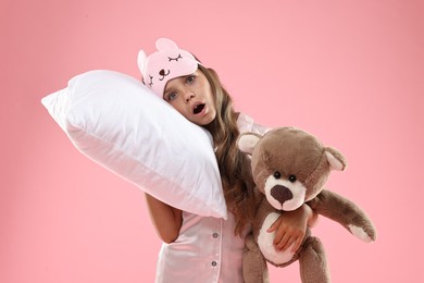 Photo of Overslept girl with sleep mask, pillow and teddy bear on pink background