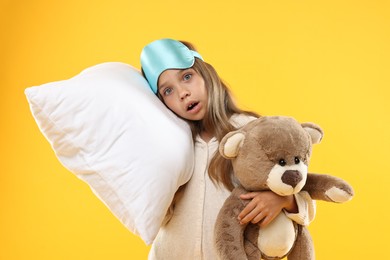 Photo of Overslept girl with sleep mask, pillow and teddy bear on orange background