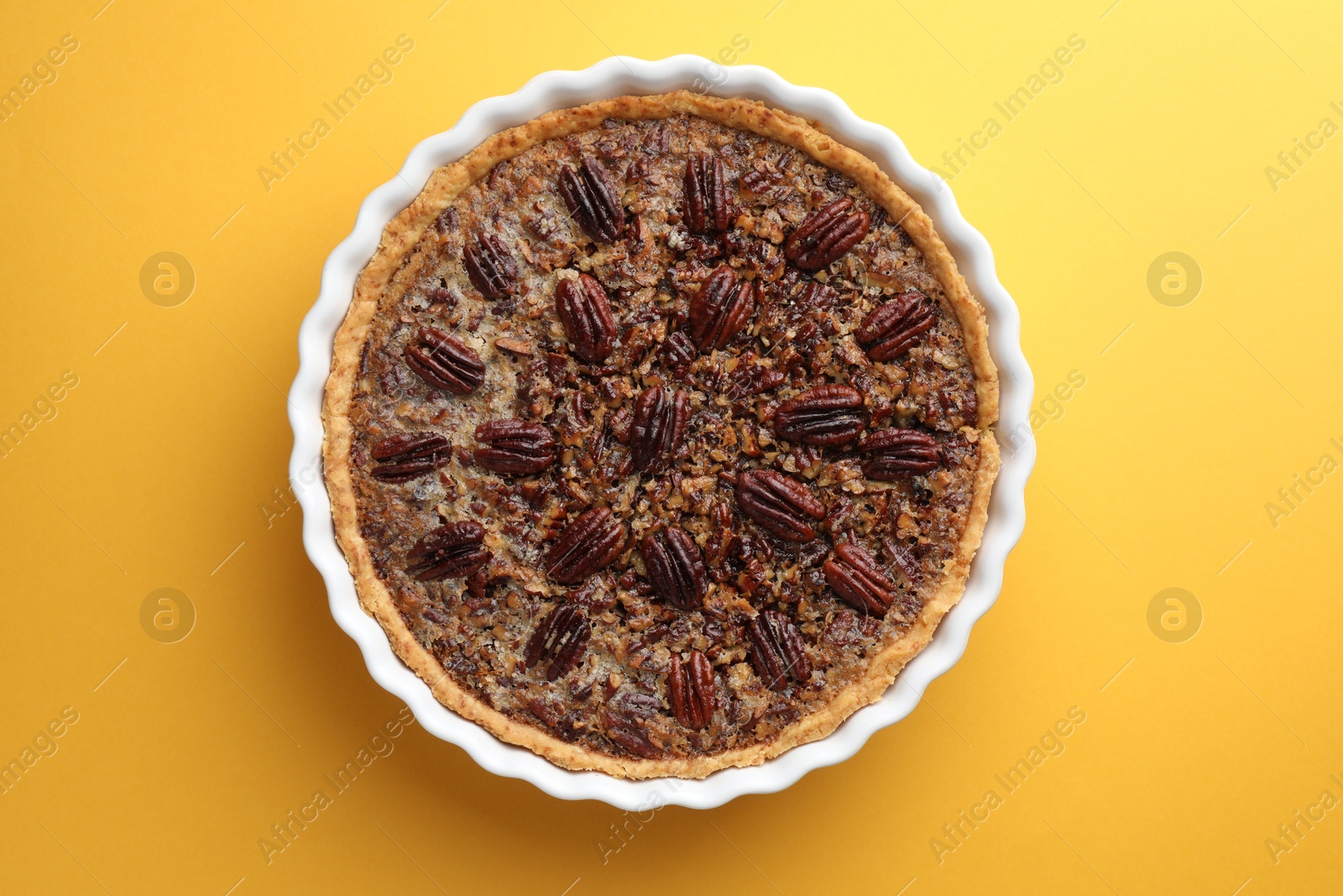 Photo of Delicious pecan pie in baking dish on yellow background, top view