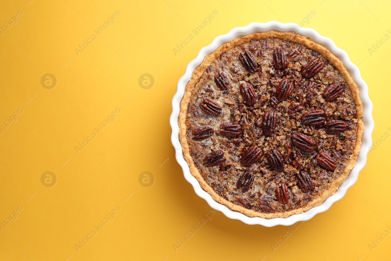 Photo of Delicious pecan pie in baking dish on yellow background, top view. Space for text