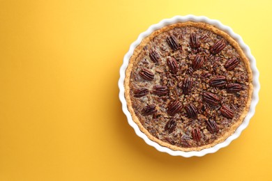 Delicious pecan pie in baking dish on yellow background, top view. Space for text