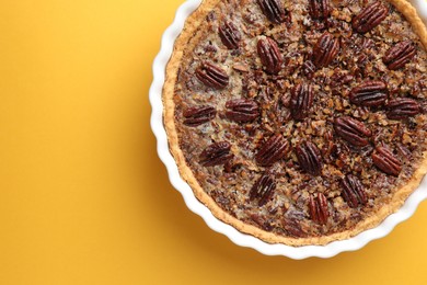 Photo of Delicious pecan pie in baking dish on yellow background, top view. Space for text