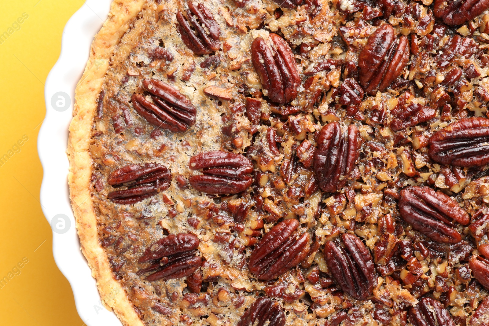 Photo of Delicious pecan pie in baking dish on yellow background, top view