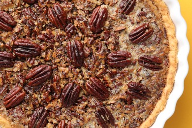 Photo of Delicious pecan pie in baking dish on yellow background, top view