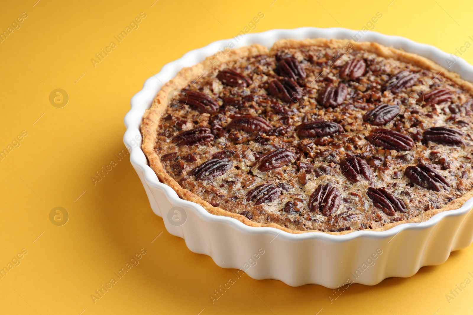 Photo of Delicious pecan pie in baking dish on yellow background, closeup