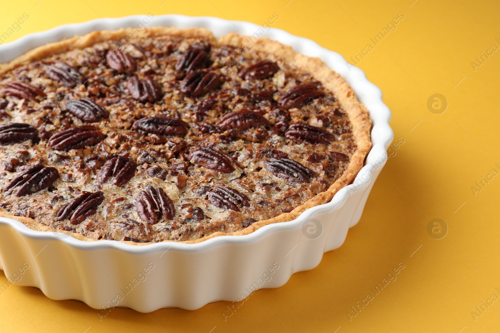 Photo of Delicious pecan pie in baking dish on yellow background, closeup