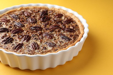 Delicious pecan pie in baking dish on yellow background, closeup