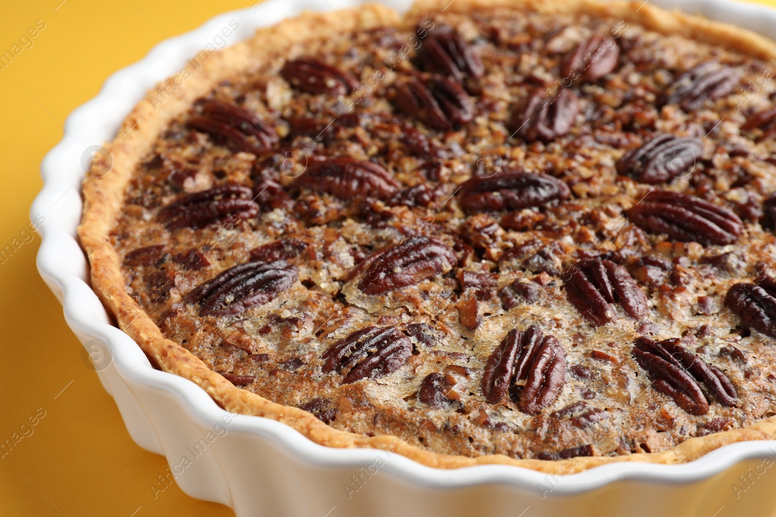 Photo of Delicious pecan pie in baking dish on yellow background, closeup