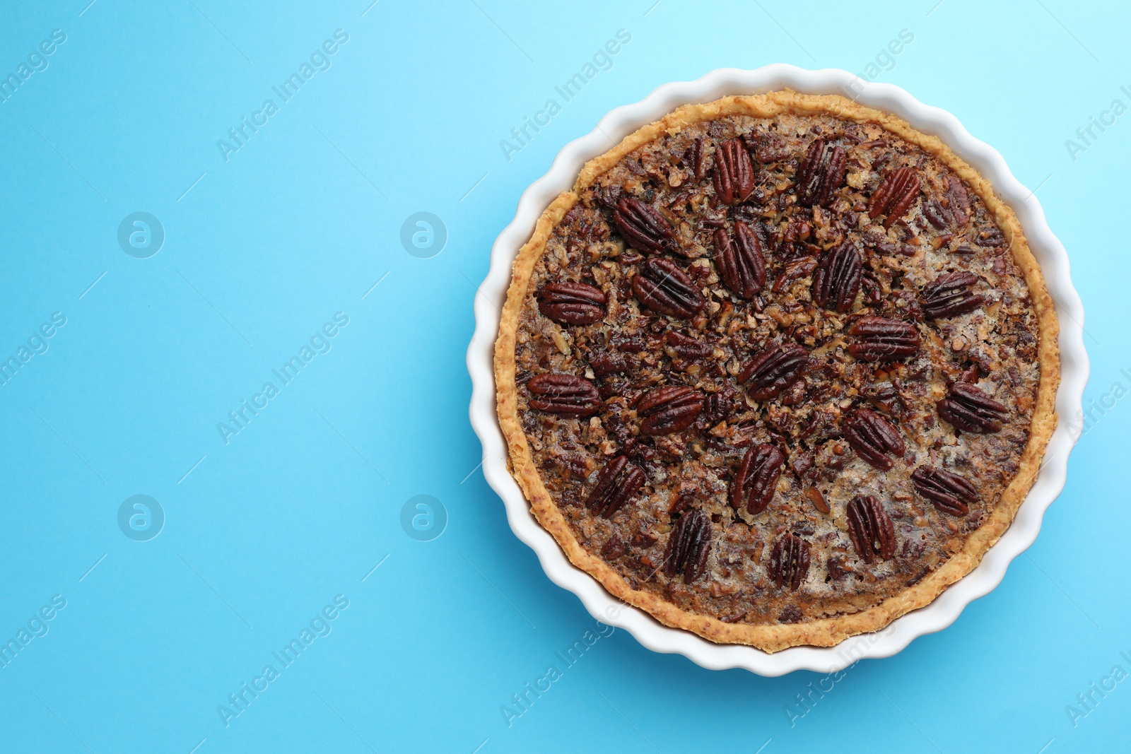 Photo of Delicious pecan pie in baking dish on light blue background, top view. Space for text