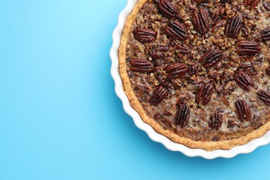 Delicious pecan pie in baking dish on light blue background, top view. Space for text