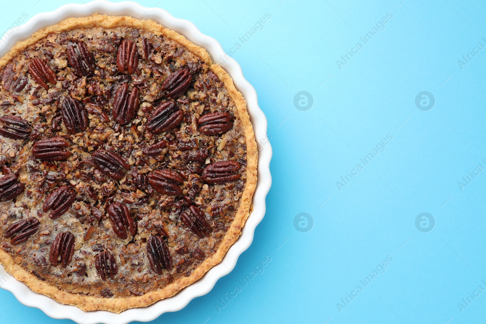 Photo of Delicious pecan pie in baking dish on light blue background, top view. Space for text