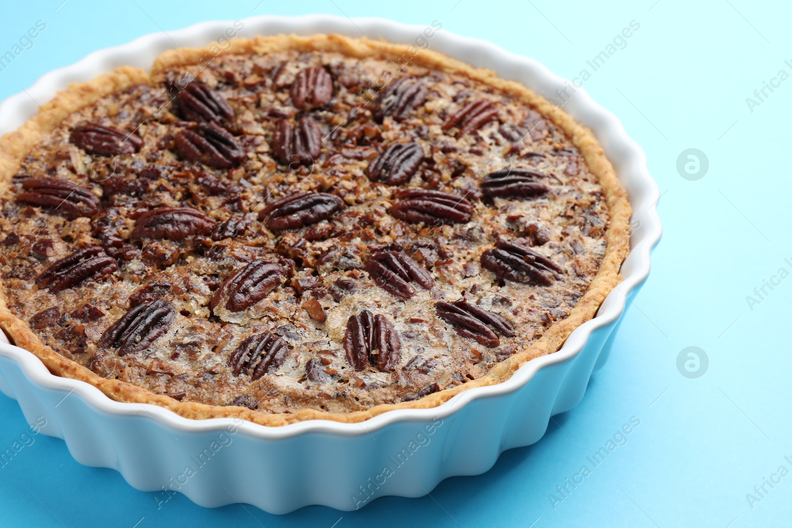 Photo of Delicious pecan pie in baking dish on light blue background, closeup