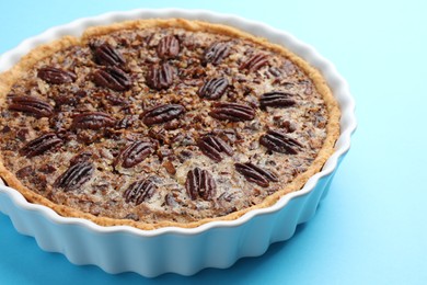 Delicious pecan pie in baking dish on light blue background, closeup