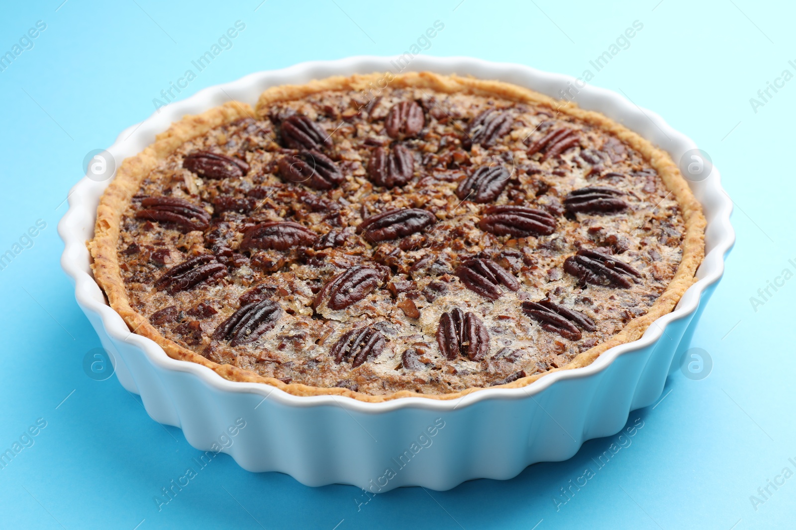 Photo of Delicious pecan pie in baking dish on light blue background, closeup