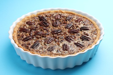 Photo of Delicious pecan pie in baking dish on light blue background, closeup