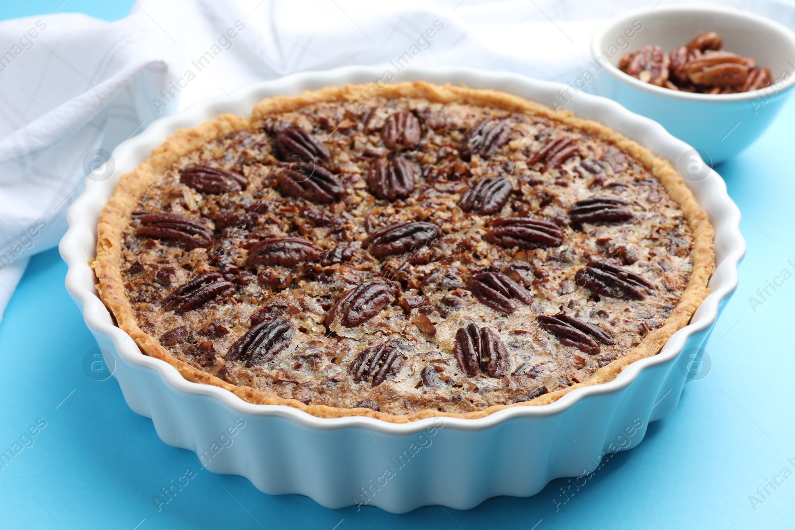 Photo of Delicious pecan pie in baking dish on light blue background, closeup