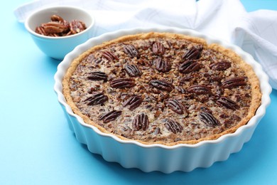 Photo of Delicious pecan pie in baking dish on light blue background, closeup